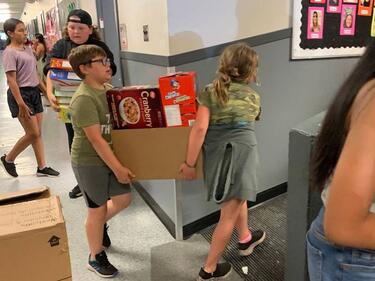 Two students carrying a box full of cereal boxes