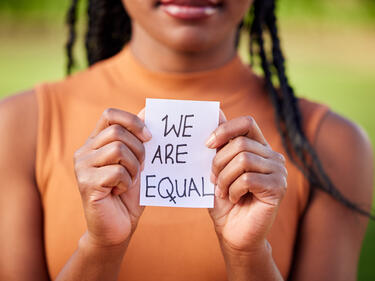 Out of focus women holds piece of paper that says "we are equal"
