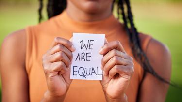 Out of focus women holds piece of paper that says "we are equal"