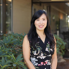 Women stands outside in front of building with greenery in the background
